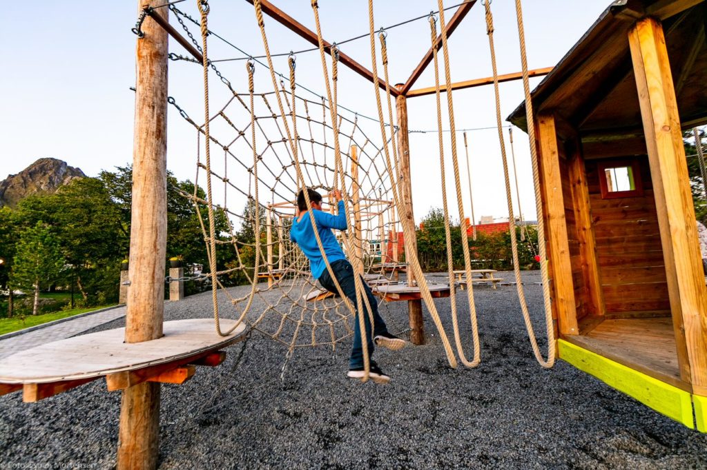 Children climb on a playground with wooden climbing elements and natural rope.
